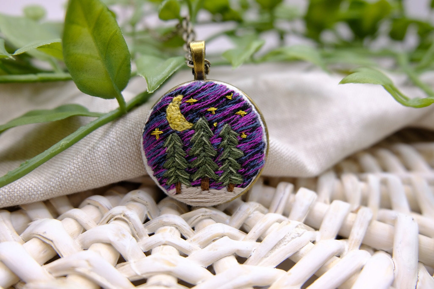 Embroidered bronze pendant featuring evergreen trees, a night sky with stars, moon and snow