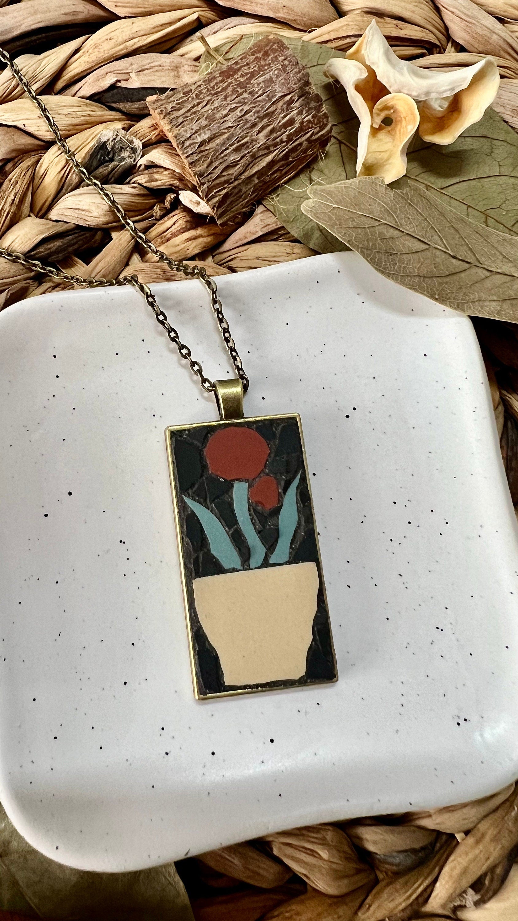 Bronze rectangular pendant with a mosaic red flower in a tan pot set in a black background