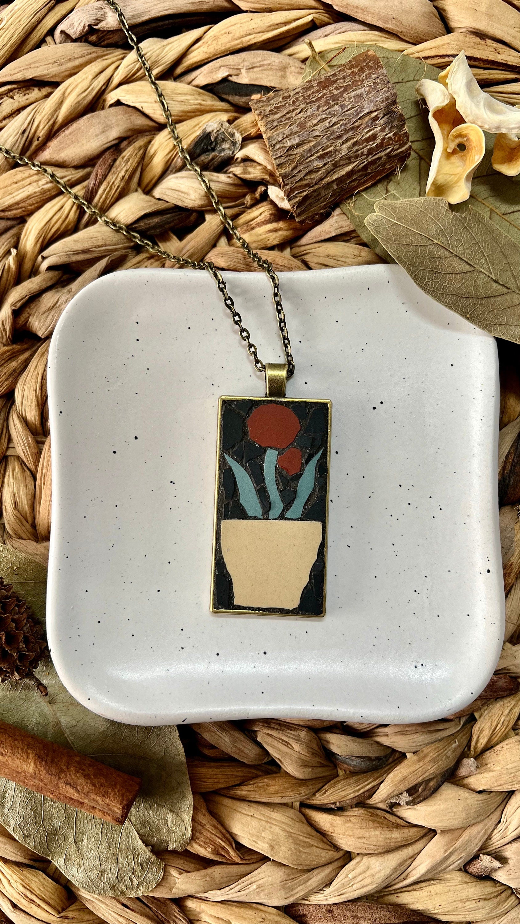 Bronze rectangular pendant with a mosaic red flower in a tan pot set in a black background