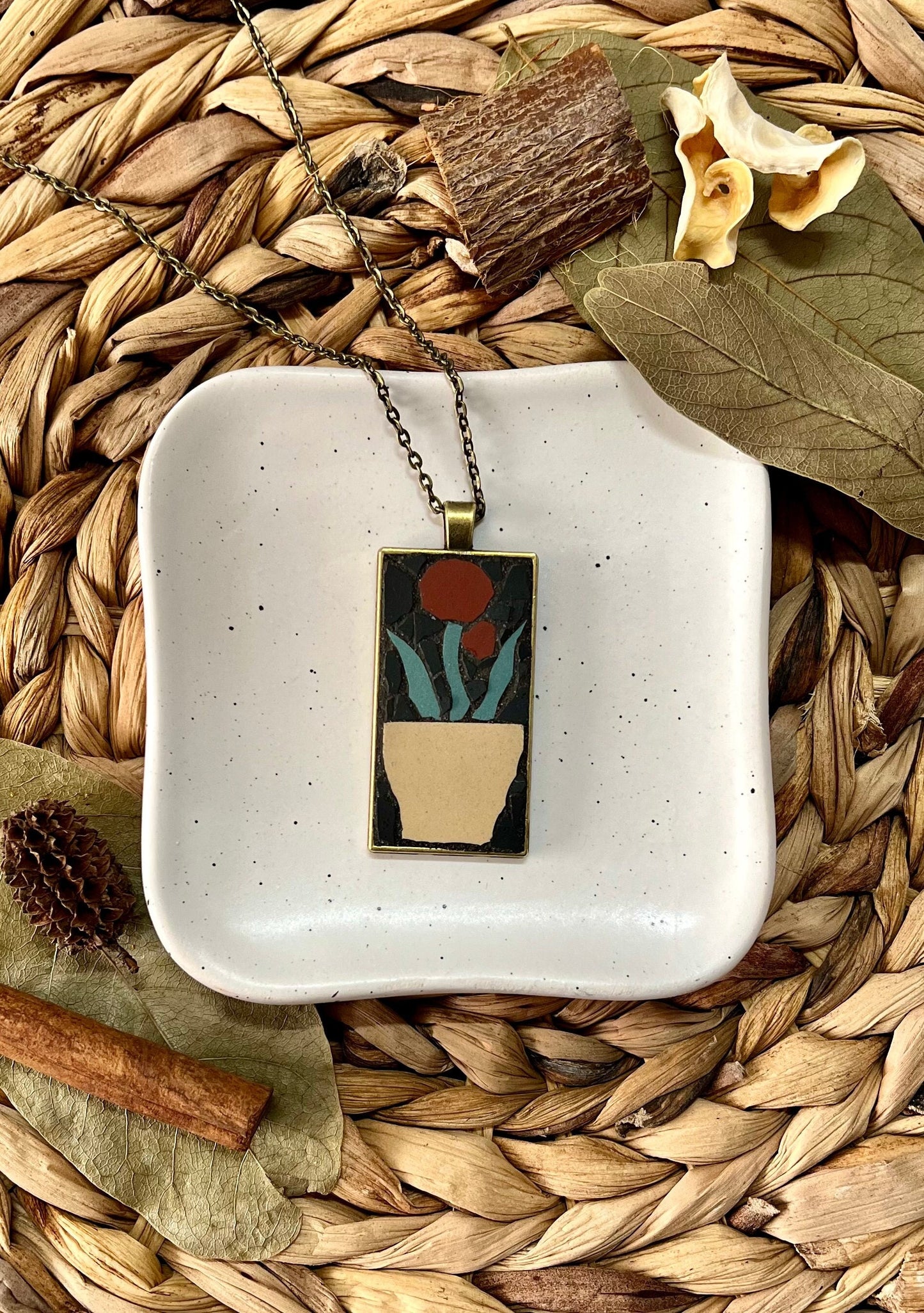 Bronze rectangular pendant with a mosaic red flower in a tan pot set in a black background