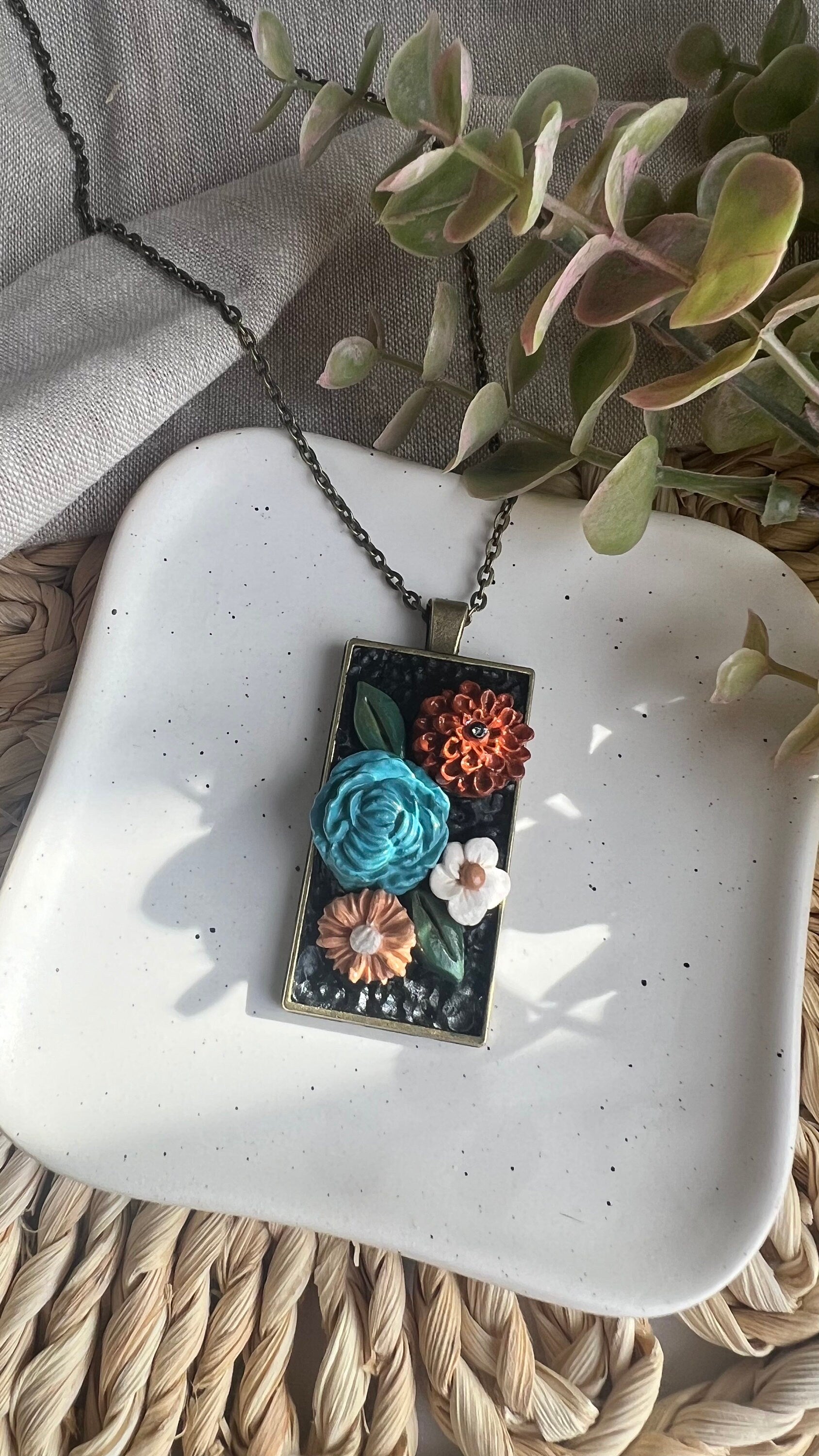 Bronze rectangular bezel with hade made clay florals on a black background