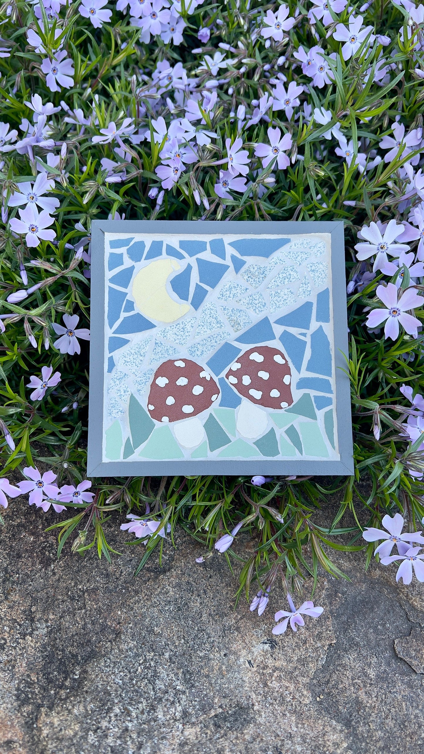 Framed mosaic art featuring two red mushrooms in a night sky with a yellow moon, framed in gray painted wood