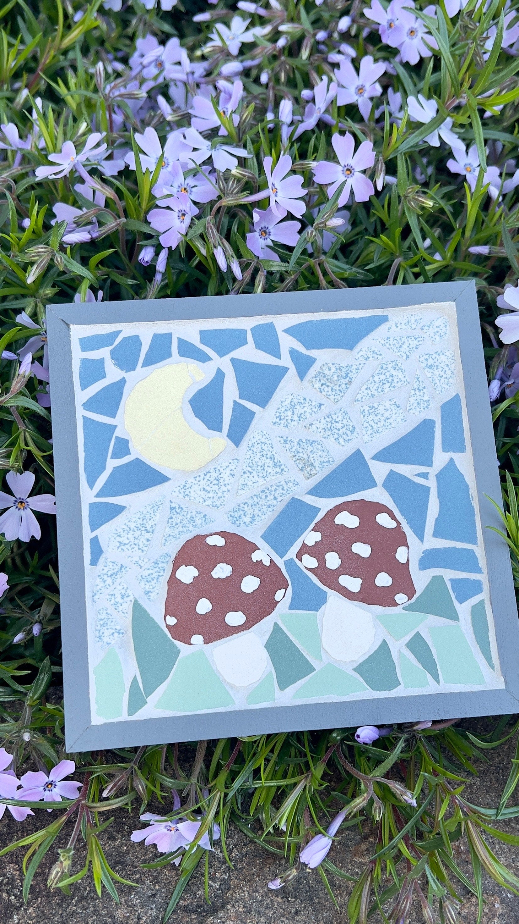 Framed mosaic art featuring two red mushrooms in a night sky with a yellow moon, framed in gray painted wood