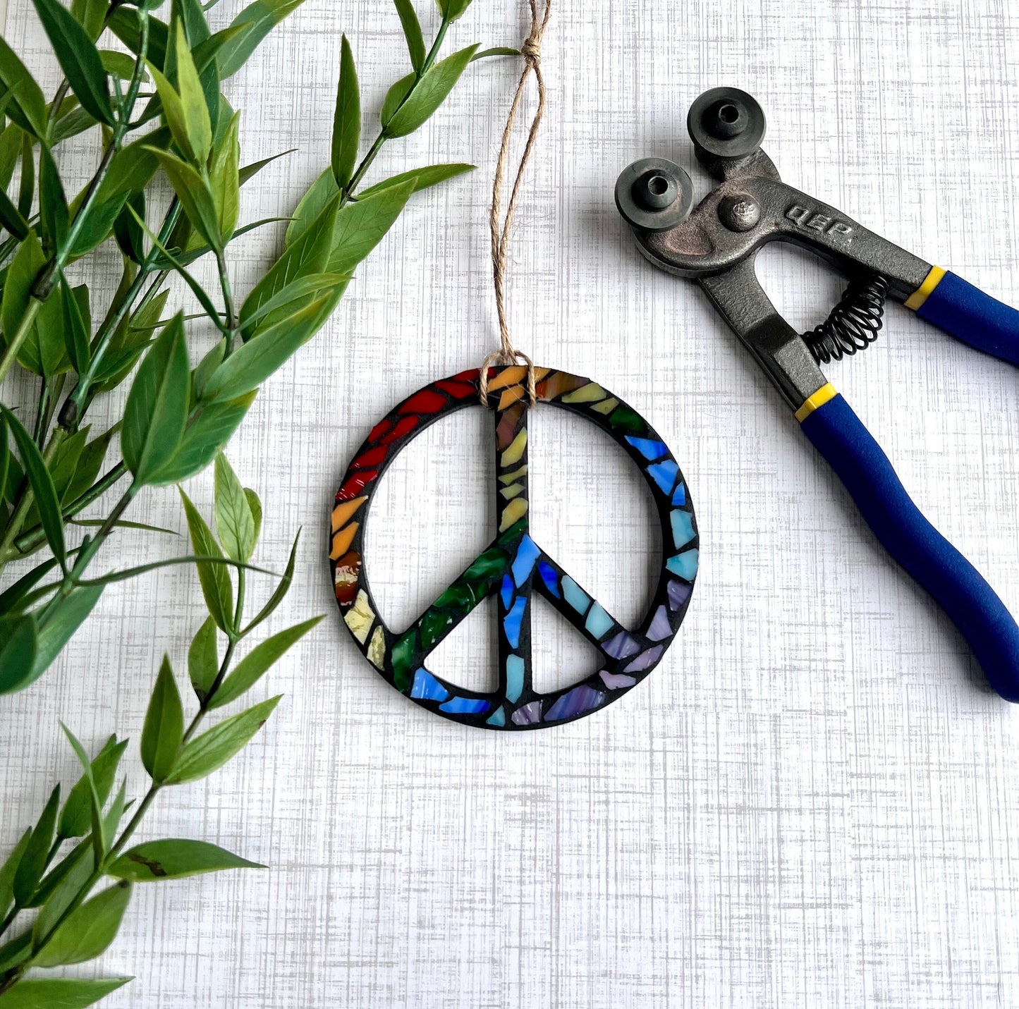 Wooden peace sign ornament with rainbow stained glass grouted in black.