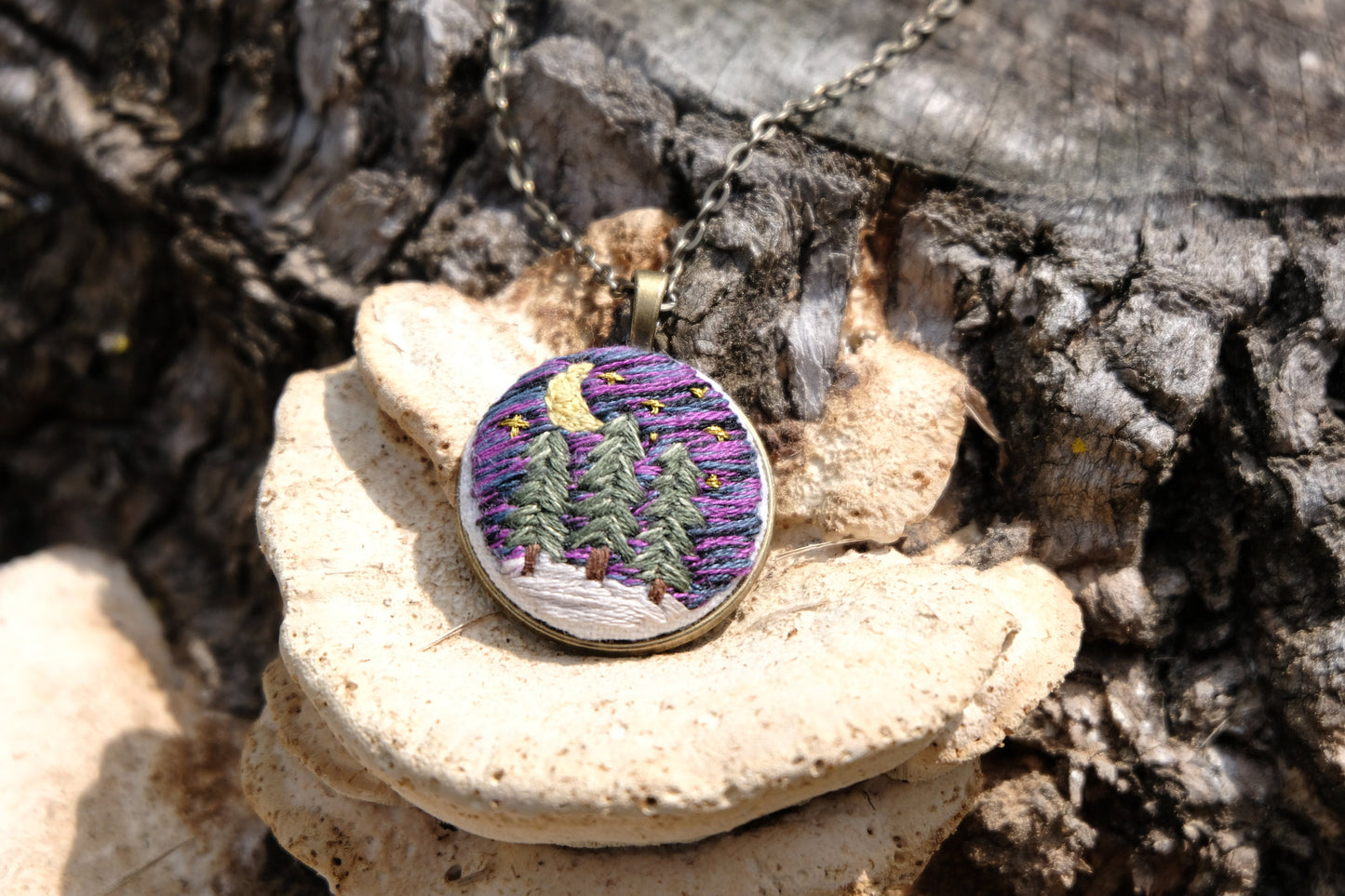 Embroidered bronze pendant featuring evergreen trees, a night sky with stars, moon and snow