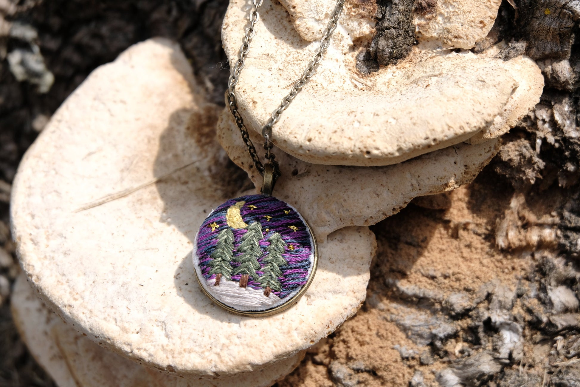 Embroidered bronze pendant featuring evergreen trees, a night sky with stars, moon and snow