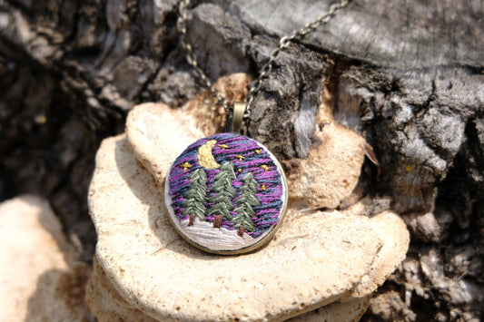 Embroidered bronze pendant featuring evergreen trees, a night sky with stars, moon and snow