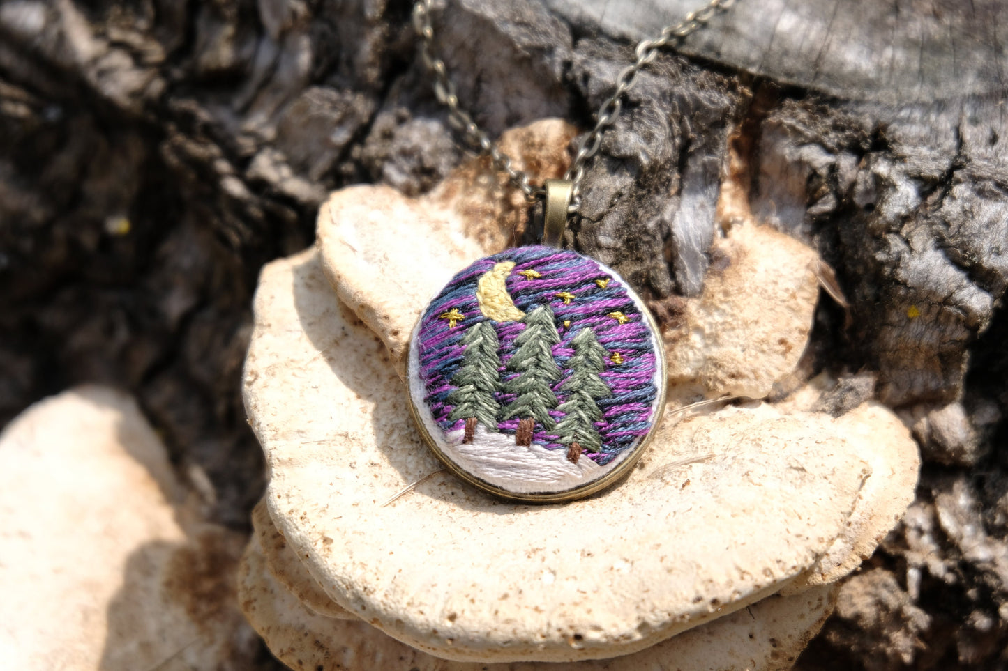 Embroidered bronze pendant featuring evergreen trees, a night sky with stars, moon and snow